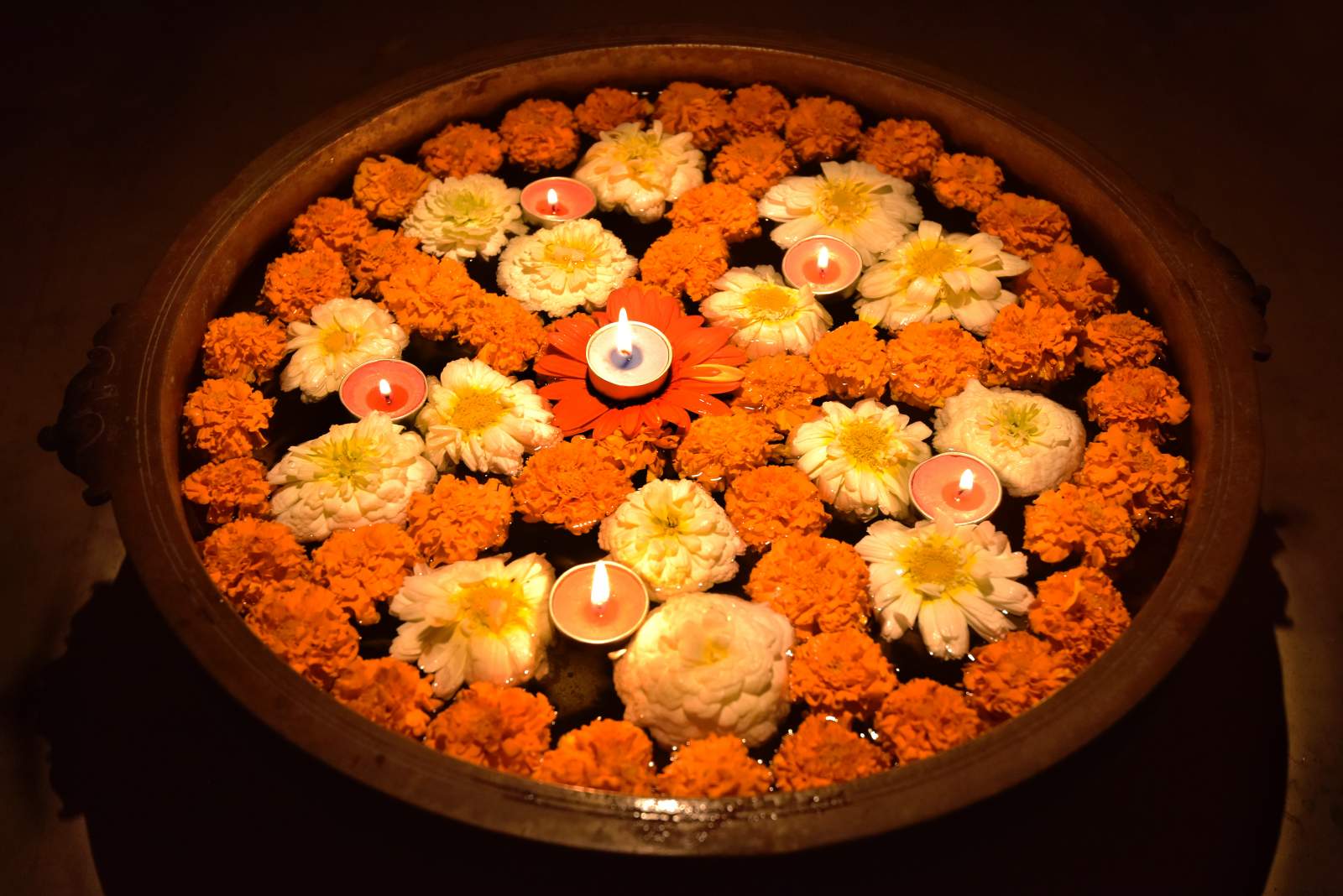 Tea light candles, surrounded by orange and yellow flowers, floating in a bowl of water