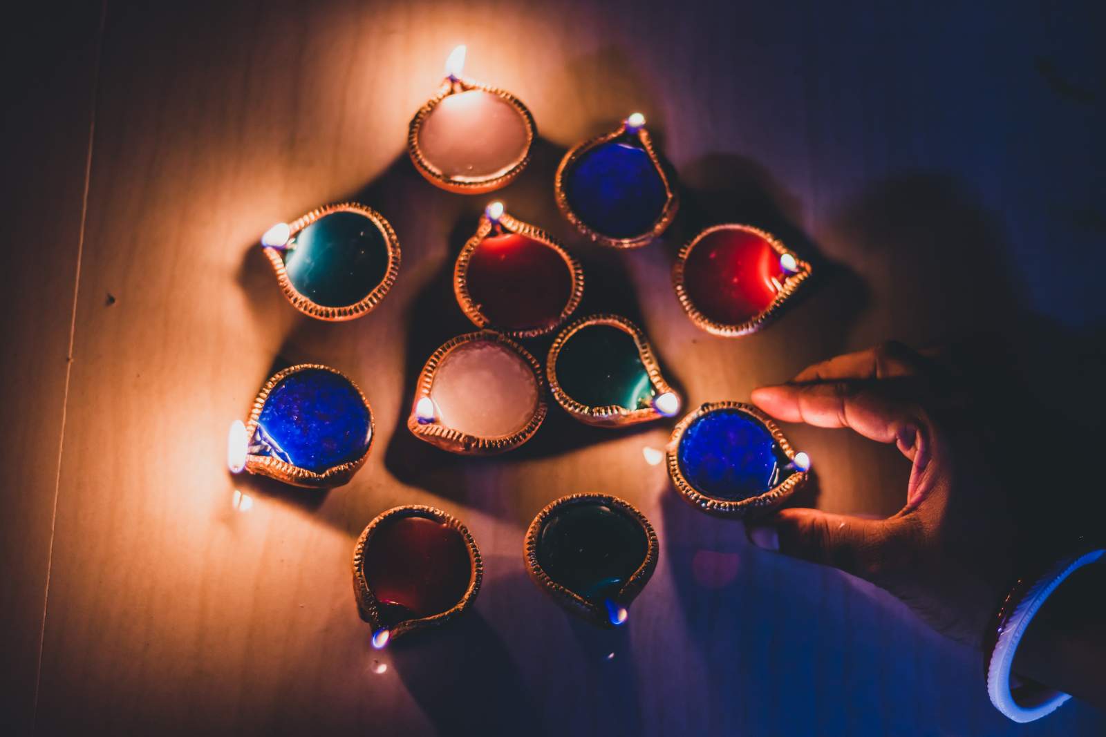Lit candles in the shape of teardrops, arranged in a circle with a hand placing the final one