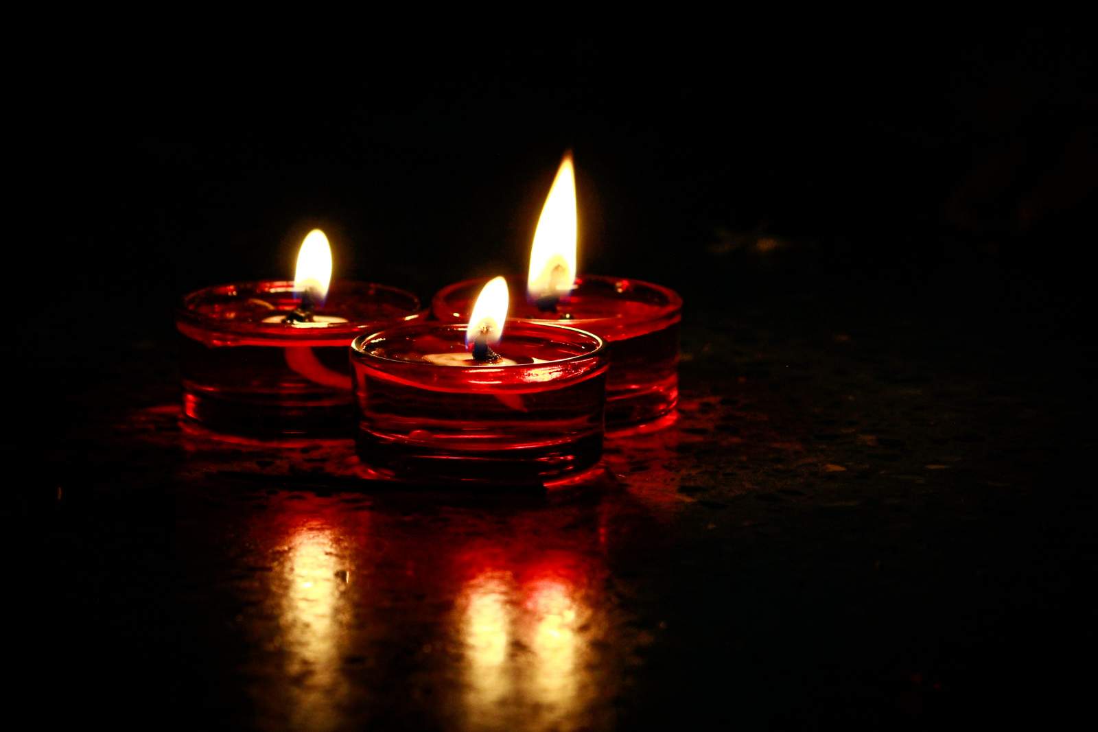 Lit candles in the shape of teardrops, arranged in a circle with a hand placing the final one