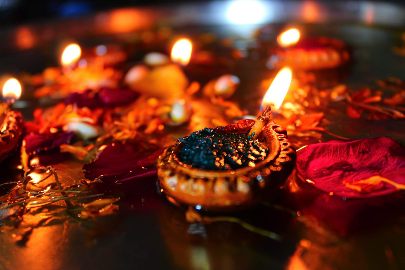 A lit colourful oil candle surrounded by flower petals